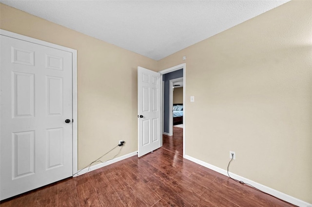 unfurnished bedroom with baseboards and dark wood-type flooring