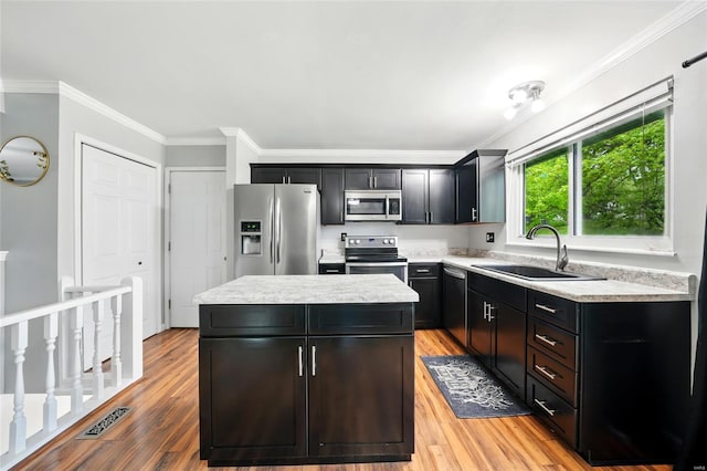 kitchen with a sink, crown molding, a kitchen island, light wood-style floors, and stainless steel appliances