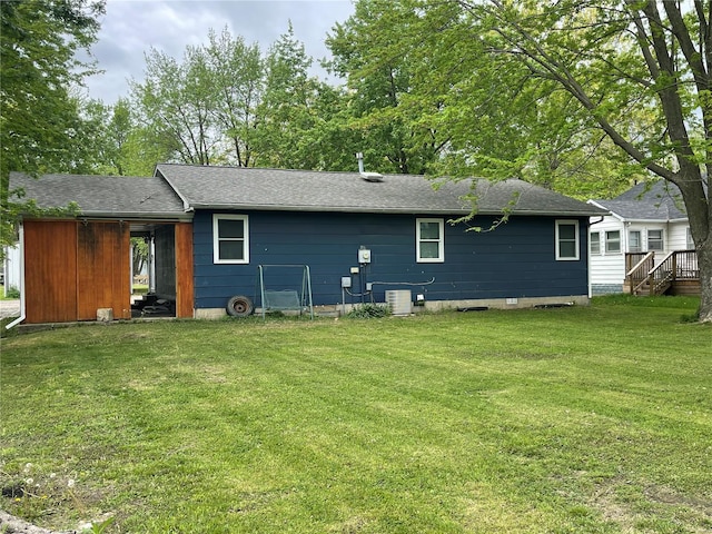 rear view of property with cooling unit, a yard, and roof with shingles