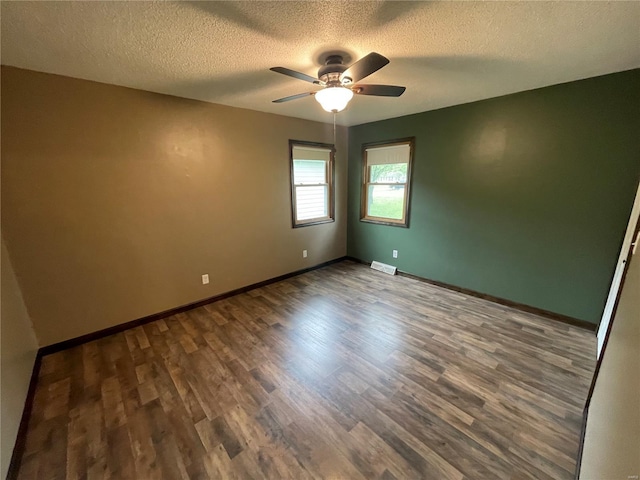 empty room with a textured ceiling, wood finished floors, a ceiling fan, and visible vents