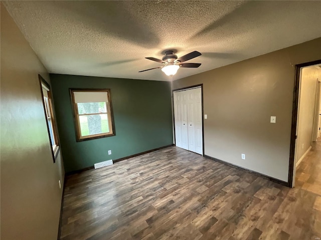 unfurnished bedroom with dark wood-style floors, a ceiling fan, visible vents, baseboards, and a textured ceiling