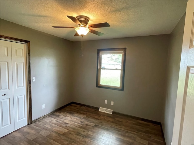 spare room featuring baseboards, dark wood-style floors, visible vents, a ceiling fan, and a textured ceiling
