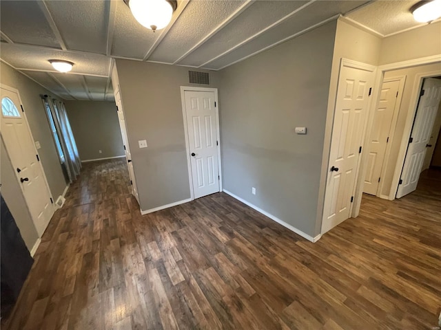 unfurnished room featuring a textured ceiling, visible vents, dark wood-style flooring, and baseboards