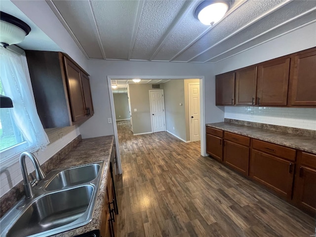kitchen with a sink, decorative backsplash, dark countertops, a textured ceiling, and dark wood finished floors
