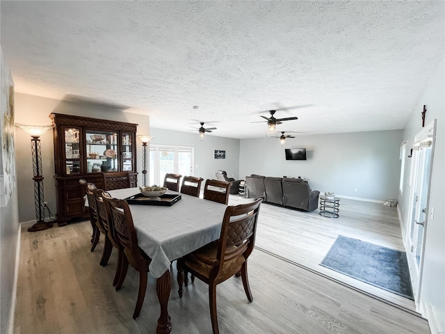 dining space with baseboards, a textured ceiling, and light wood-style flooring