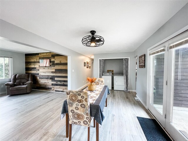 dining area with light wood finished floors, baseboards, wood walls, and washer and clothes dryer