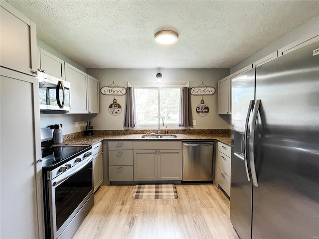kitchen featuring dark countertops, stainless steel appliances, light wood-type flooring, and a sink