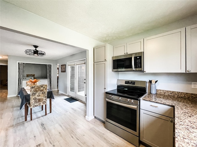 kitchen featuring a textured ceiling, dark stone countertops, light wood-type flooring, baseboards, and appliances with stainless steel finishes