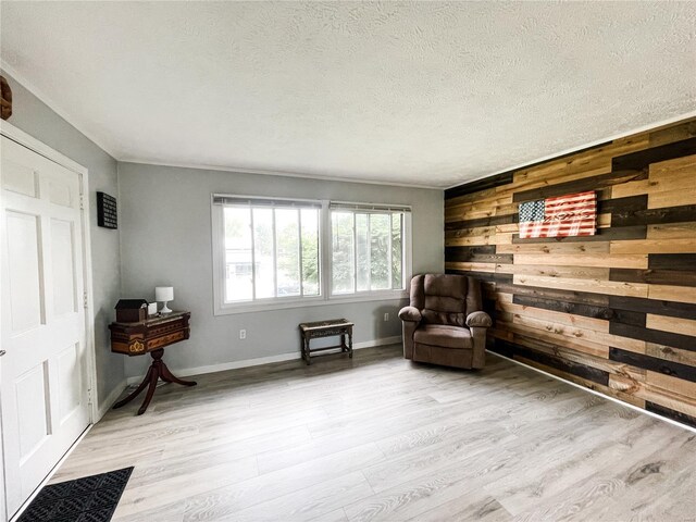 living area featuring crown molding, wood finished floors, a textured ceiling, wooden walls, and baseboards