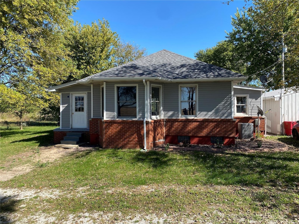 bungalow-style house featuring entry steps, a shingled roof, a front lawn, and brick siding