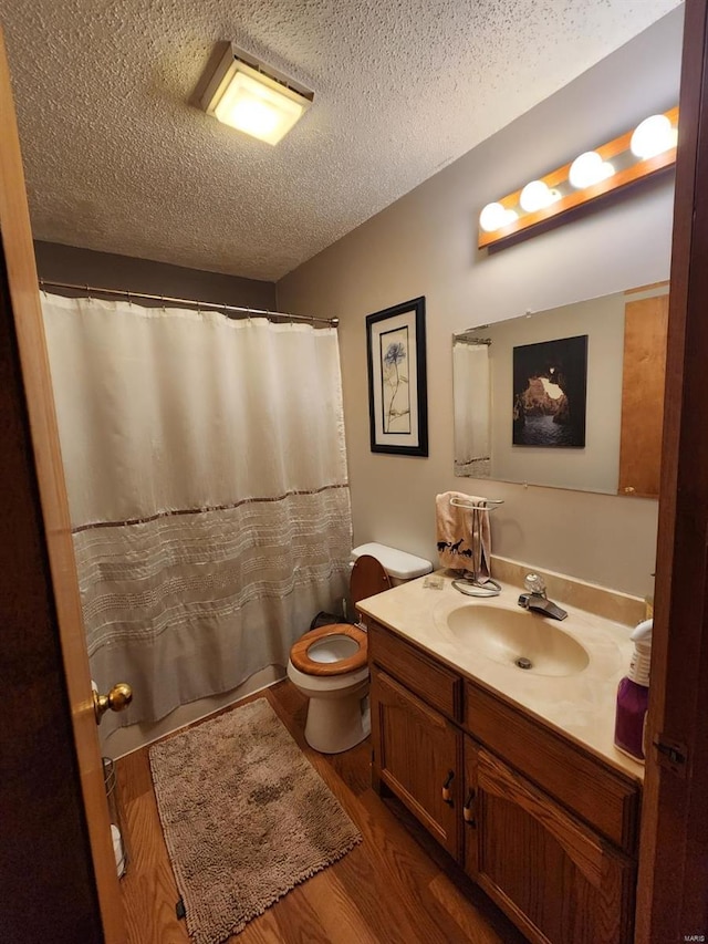 full bath with a textured ceiling, a shower with shower curtain, toilet, wood finished floors, and vanity