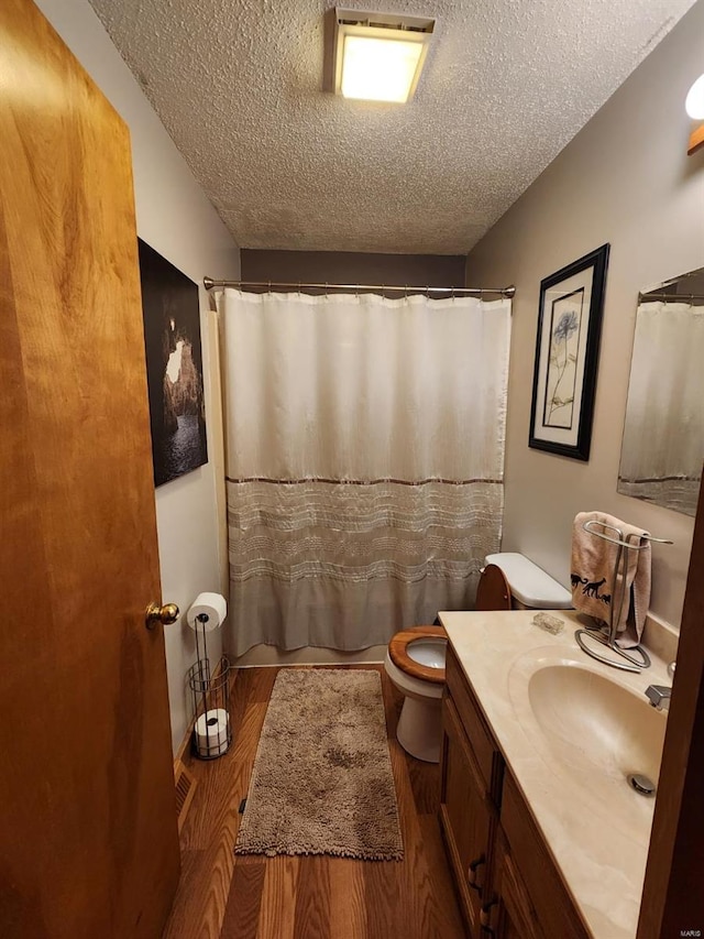 full bathroom with wood finished floors, a shower with curtain, toilet, vanity, and a textured ceiling