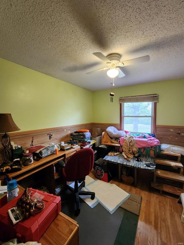bedroom featuring wood finished floors, wainscoting, wood walls, ceiling fan, and a textured ceiling
