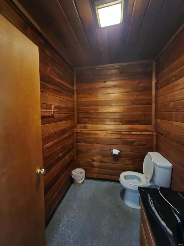 bathroom featuring toilet, concrete flooring, wood walls, and wood ceiling