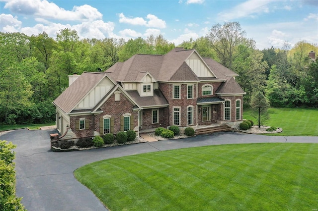 view of front of house featuring driveway, board and batten siding, a front yard, brick siding, and a forest view
