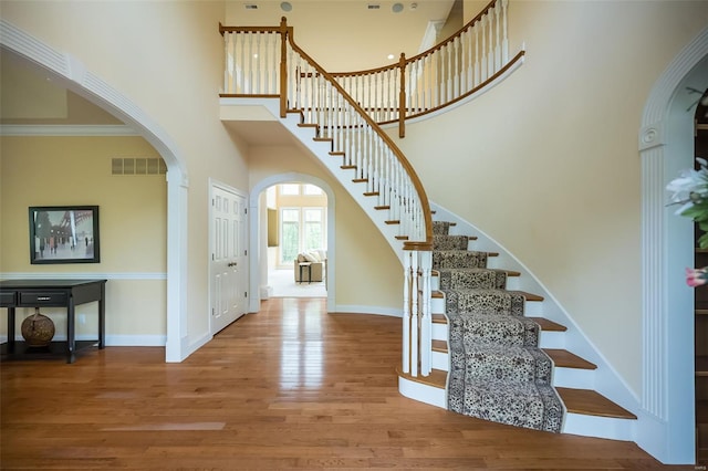 entrance foyer with a high ceiling, stairway, visible vents, arched walkways, and wood finished floors