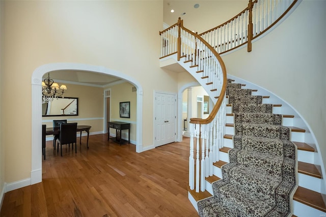 staircase featuring arched walkways, an inviting chandelier, wood finished floors, baseboards, and a high ceiling