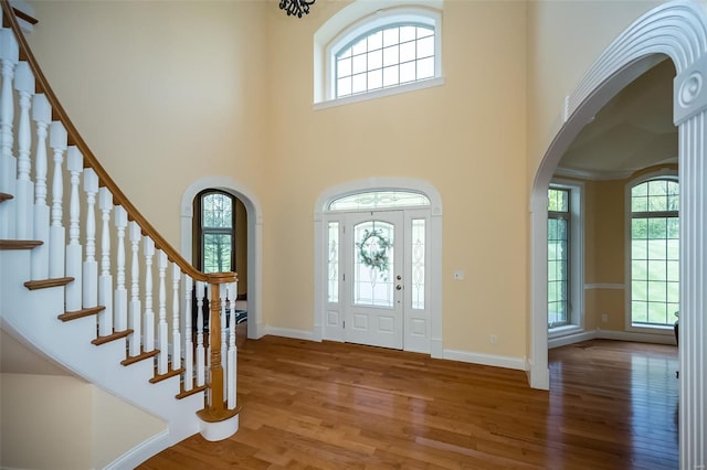 entryway featuring a high ceiling, arched walkways, wood finished floors, and plenty of natural light