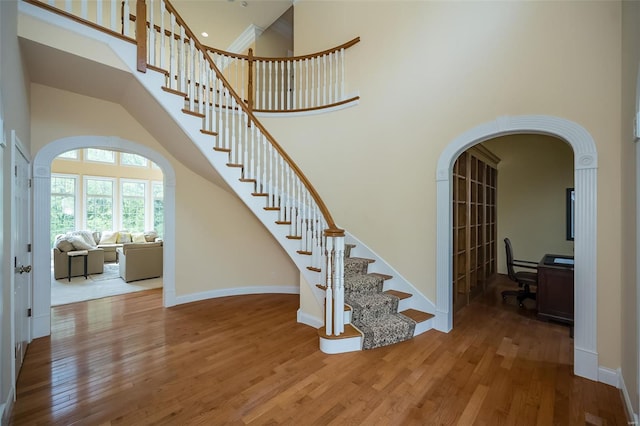 staircase featuring wood finished floors, baseboards, arched walkways, and a high ceiling