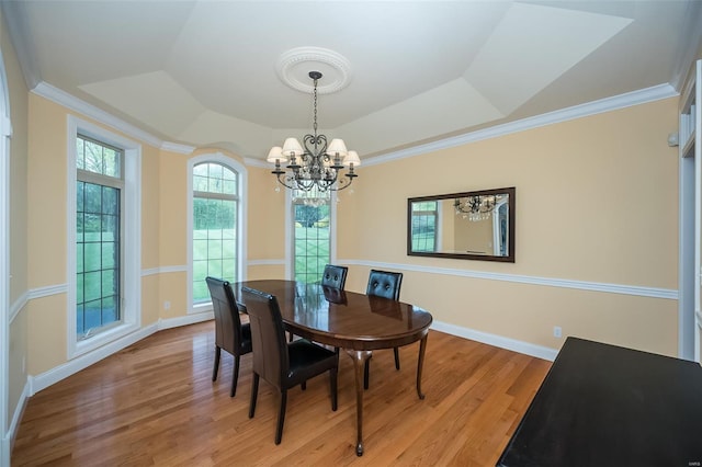 dining area with ornamental molding, a raised ceiling, a notable chandelier, and light wood-style floors