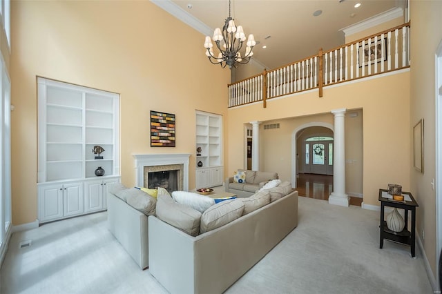 living area featuring arched walkways, light colored carpet, built in shelves, baseboards, and ornate columns