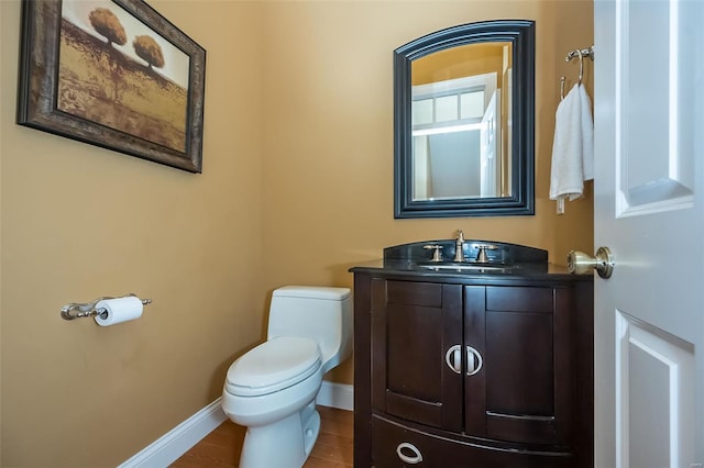half bath with toilet, wood finished floors, vanity, and baseboards