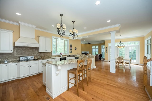 kitchen featuring white cabinetry, custom range hood, light wood-style floors, light stone countertops, and a notable chandelier