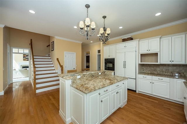 kitchen with light wood finished floors, a notable chandelier, crown molding, a center island, and white cabinetry