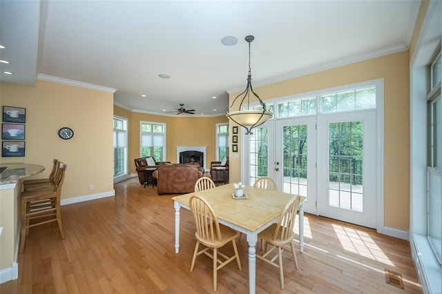 dining space with baseboards, light wood-type flooring, ornamental molding, and a fireplace