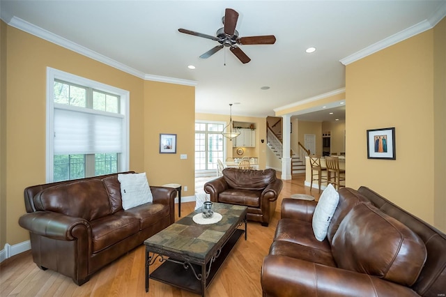 living area with stairs, light wood-style flooring, ceiling fan, baseboards, and crown molding