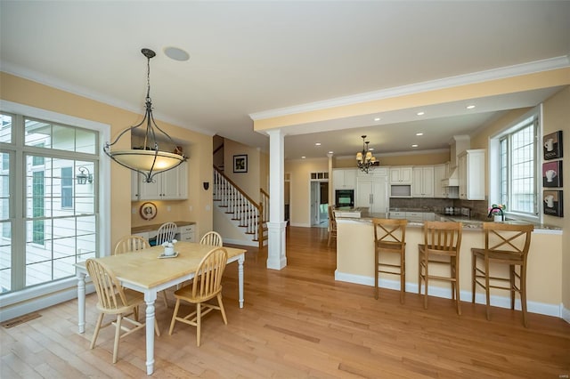 dining room with stairway, light wood-style floors, ornate columns, a notable chandelier, and crown molding