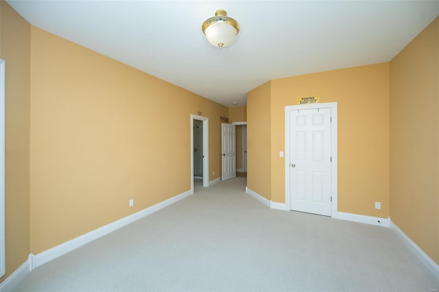 spare room featuring light colored carpet and baseboards