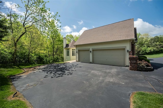 view of side of property with a chimney, aphalt driveway, and an attached garage