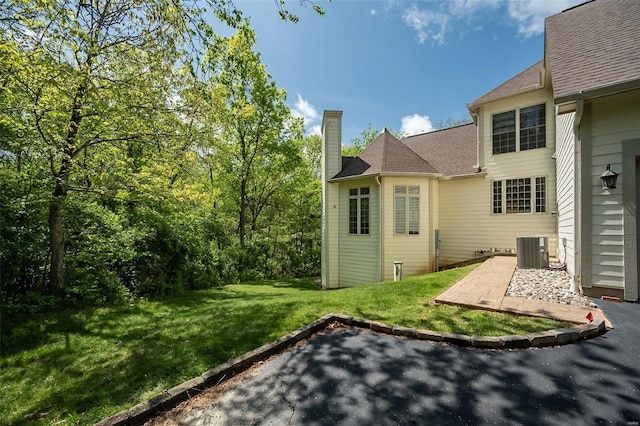 back of house featuring a chimney, a shingled roof, a patio area, central AC, and a lawn