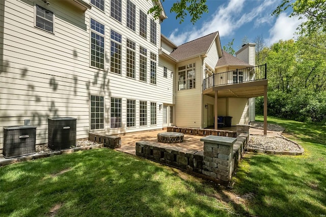 rear view of house with a fire pit, a wooden deck, central AC unit, a patio area, and a lawn
