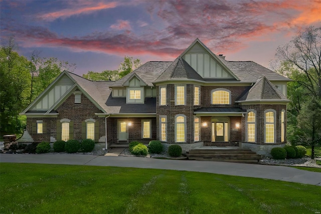 view of front facade with brick siding, board and batten siding, a front yard, and roof with shingles