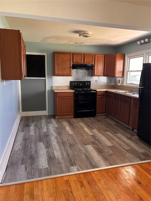 kitchen featuring black appliances, under cabinet range hood, brown cabinetry, and dark wood-style flooring