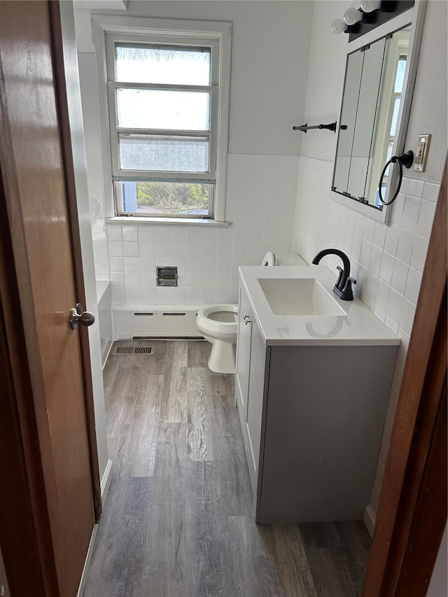 bathroom featuring a baseboard radiator, wood finished floors, tile walls, vanity, and toilet
