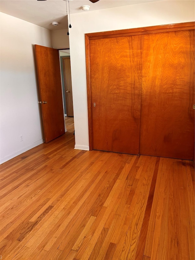unfurnished bedroom featuring light wood-type flooring, a closet, and baseboards