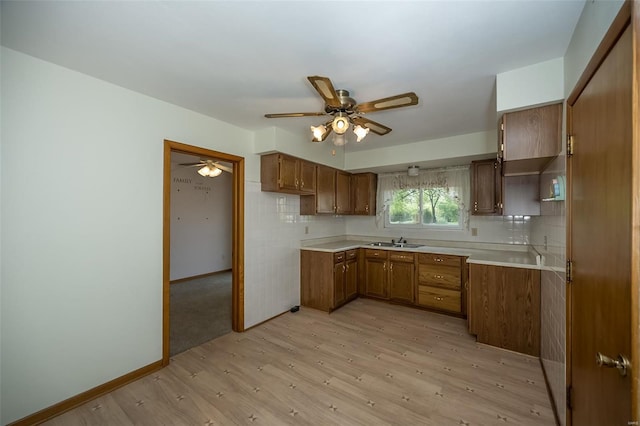 kitchen featuring light wood-type flooring, a ceiling fan, brown cabinetry, and a sink