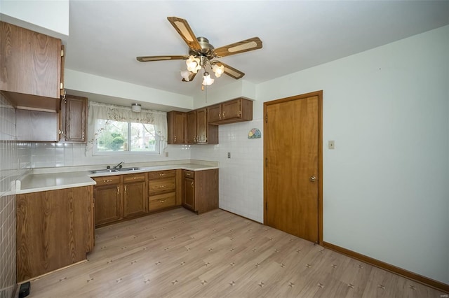 kitchen with a sink, ceiling fan, brown cabinetry, and light wood-style floors