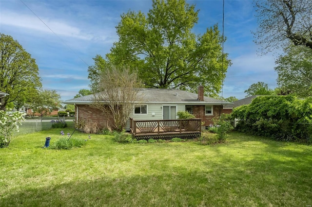 rear view of property featuring a wooden deck, a yard, a chimney, brick siding, and fence