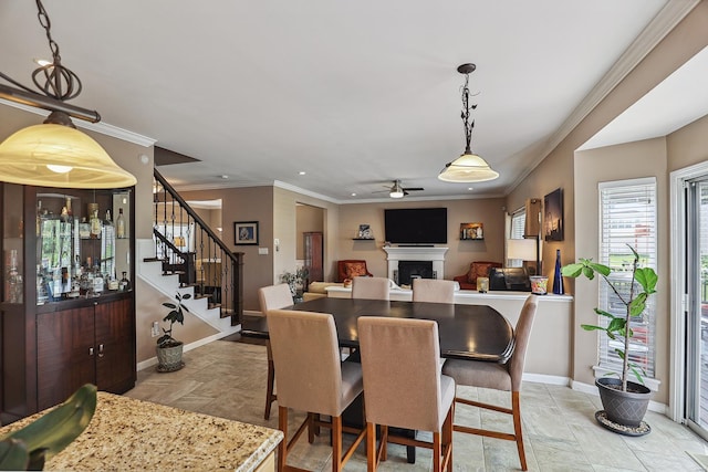 dining area featuring a ceiling fan, crown molding, a fireplace, stairway, and baseboards