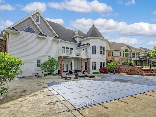 rear view of property with a balcony, a residential view, a patio area, a covered pool, and fence