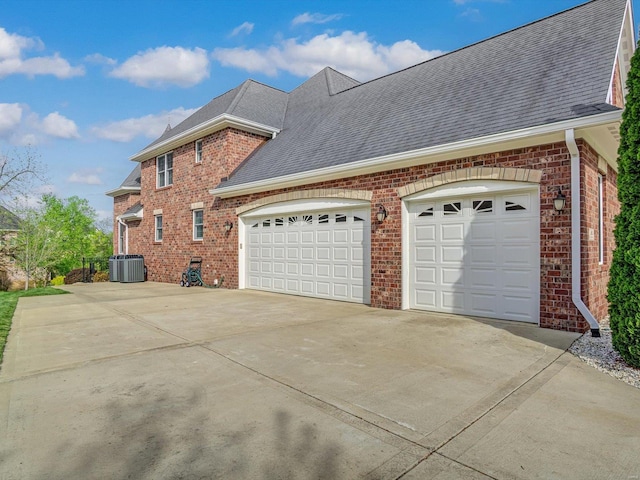 view of side of home with brick siding, cooling unit, roof with shingles, concrete driveway, and an attached garage