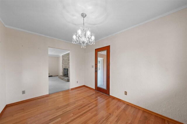 spare room with a fireplace, light wood-style flooring, a chandelier, and baseboards