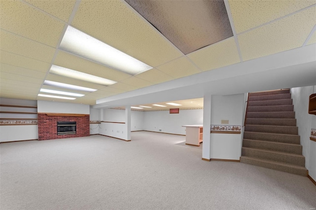 finished basement featuring carpet flooring, a fireplace, stairs, baseboards, and a drop ceiling