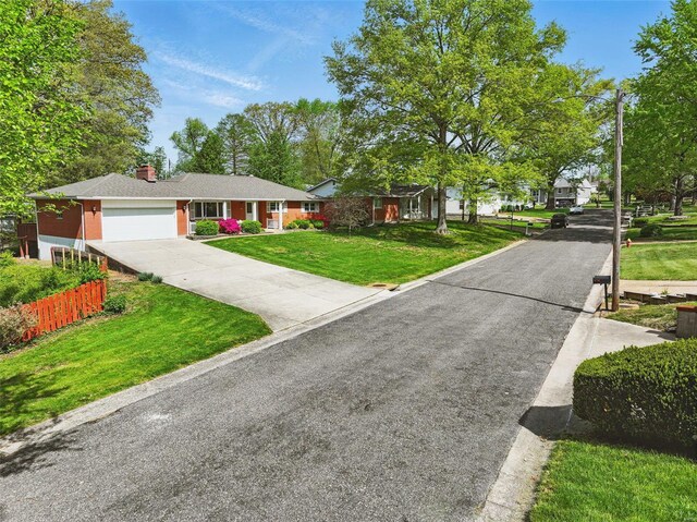single story home with a front yard, a chimney, concrete driveway, an attached garage, and fence
