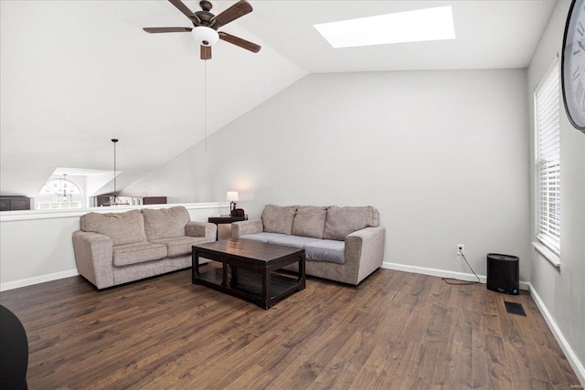 living area with dark wood finished floors, ceiling fan, a healthy amount of sunlight, and vaulted ceiling with skylight