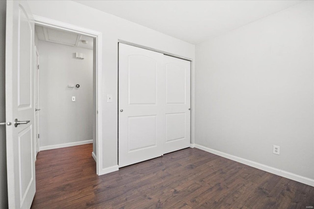 unfurnished bedroom with attic access, baseboards, a closet, and dark wood-style flooring